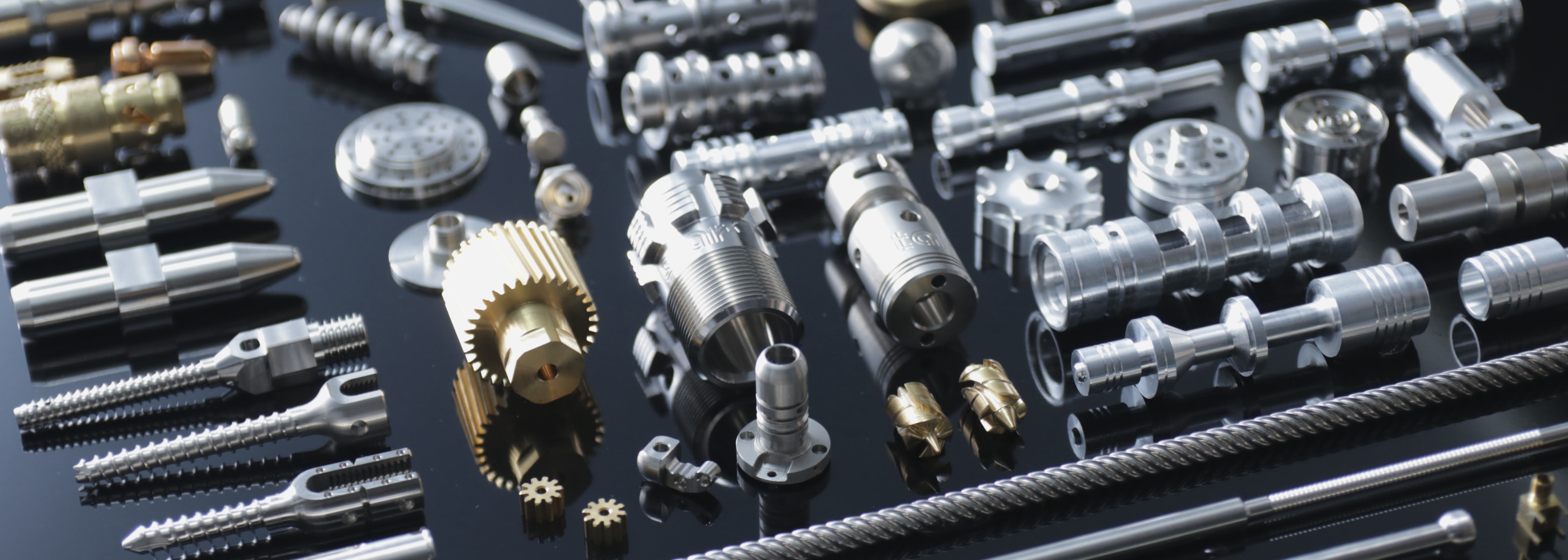 Array of precision-machined stainless, titanium and brass components on a dark reflective surface